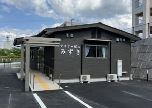 黒い外壁の介護施設の建物外観。駐車場に面した玄関入口が見える。